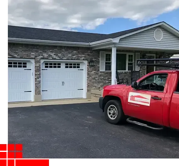 Red work truck parked by a gray stone house with two white garage doors