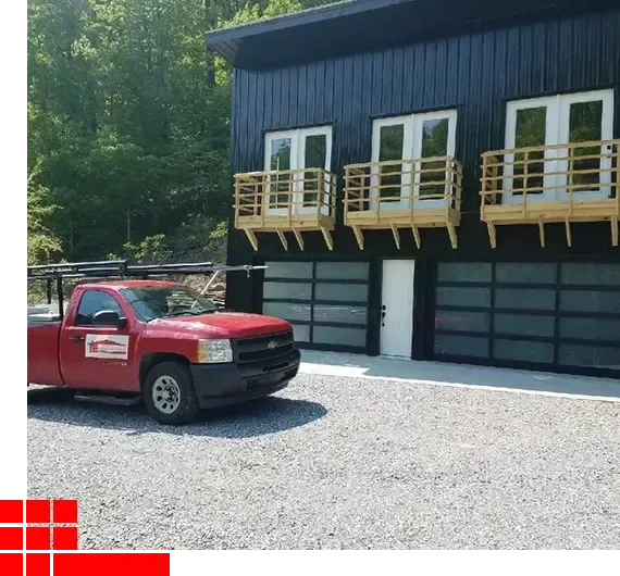 Red pickup truck parked beside a dark blue building with wooden balconies and garage doors
