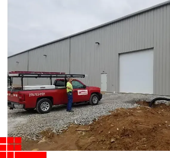 Worker beside red utility truck outside large gray metal building