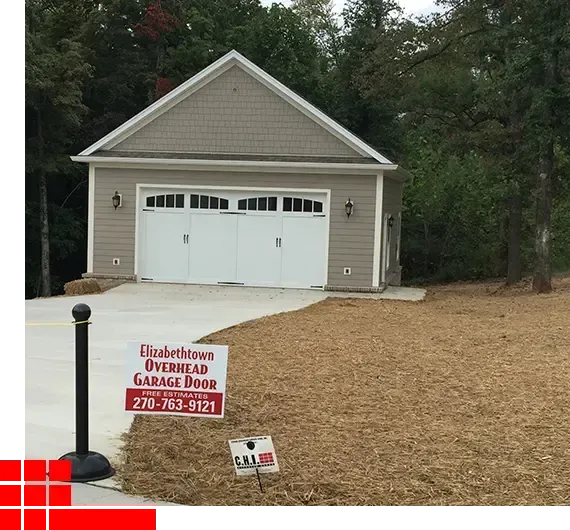 Detached beige garage with white double doors, driveway, and a red 
