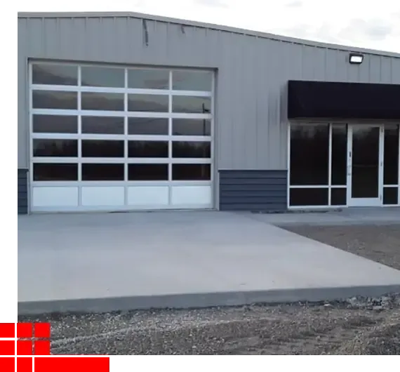 Gray industrial building with a glass garage door, entry windows, and a concrete driveway.