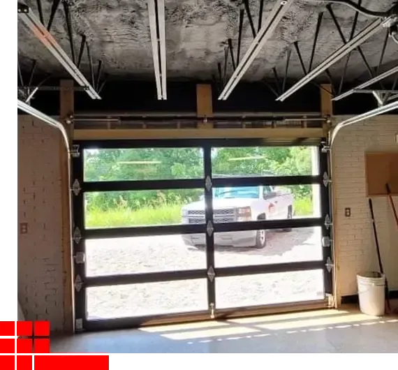 Empty garage with a glass roll-up door open to a driveway and greenery outside.