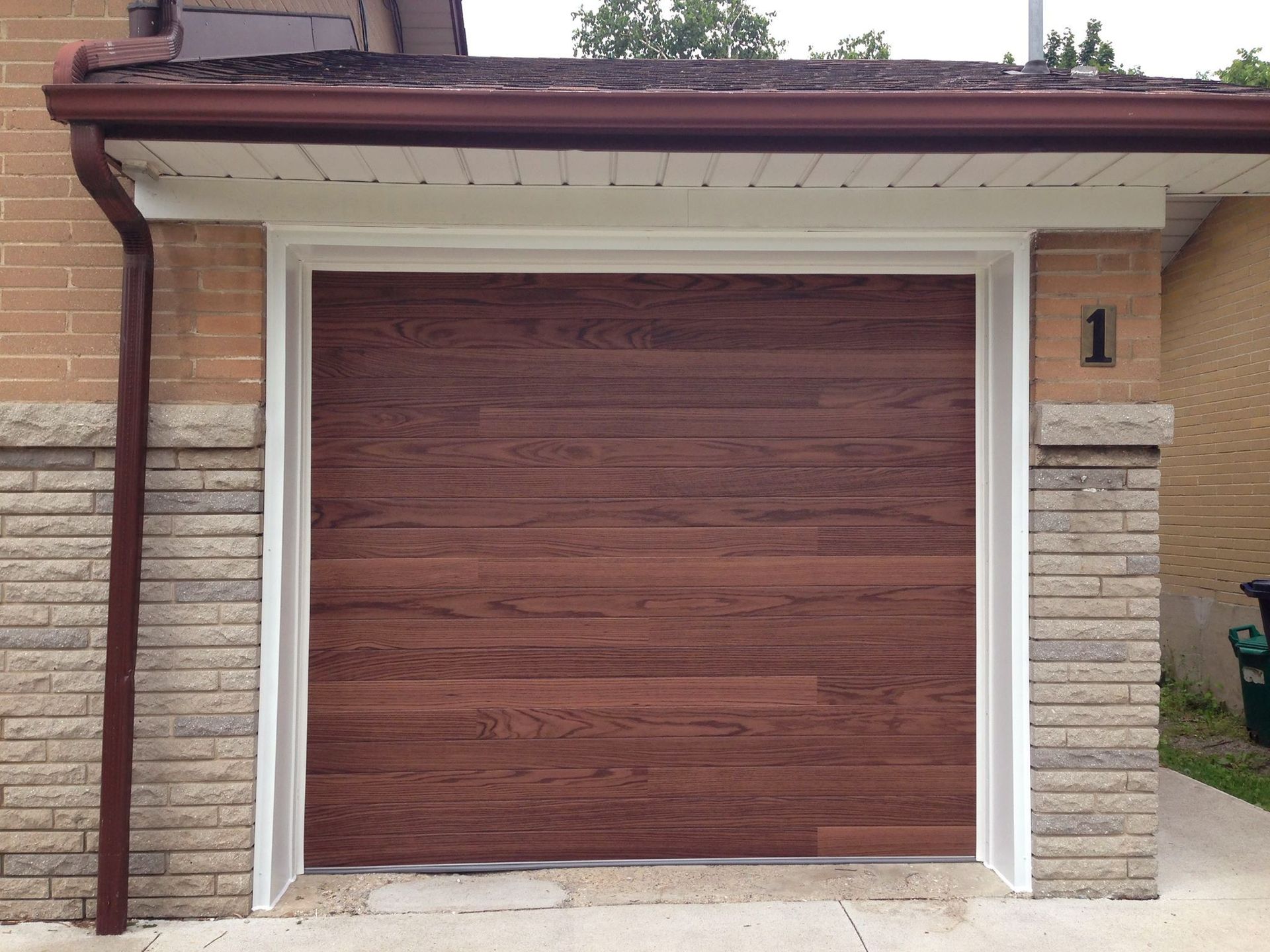 Single-car garage with a wood-paneled door and stone siding under a small roof overhang.