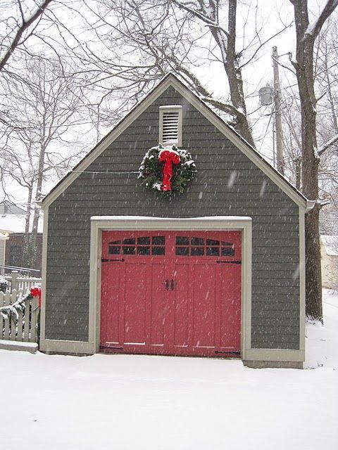 Snowy garage with red double doors and a holiday wreath above them