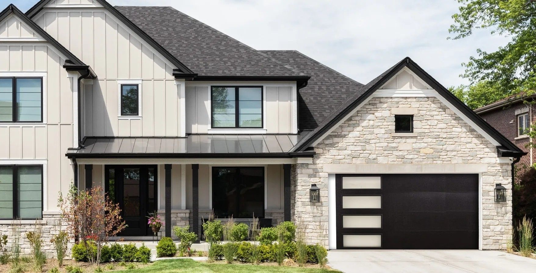 Modern two-story suburban house with beige siding, stone accents, and a black garage door
