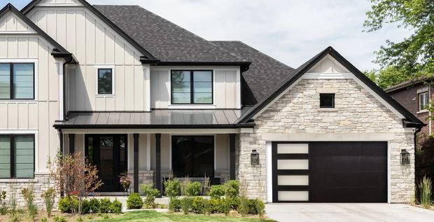 Modern two-story suburban house with beige siding, stone accents, and a black garage door