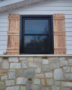 House window with black frame, wooden shutters, and stone foundation siding