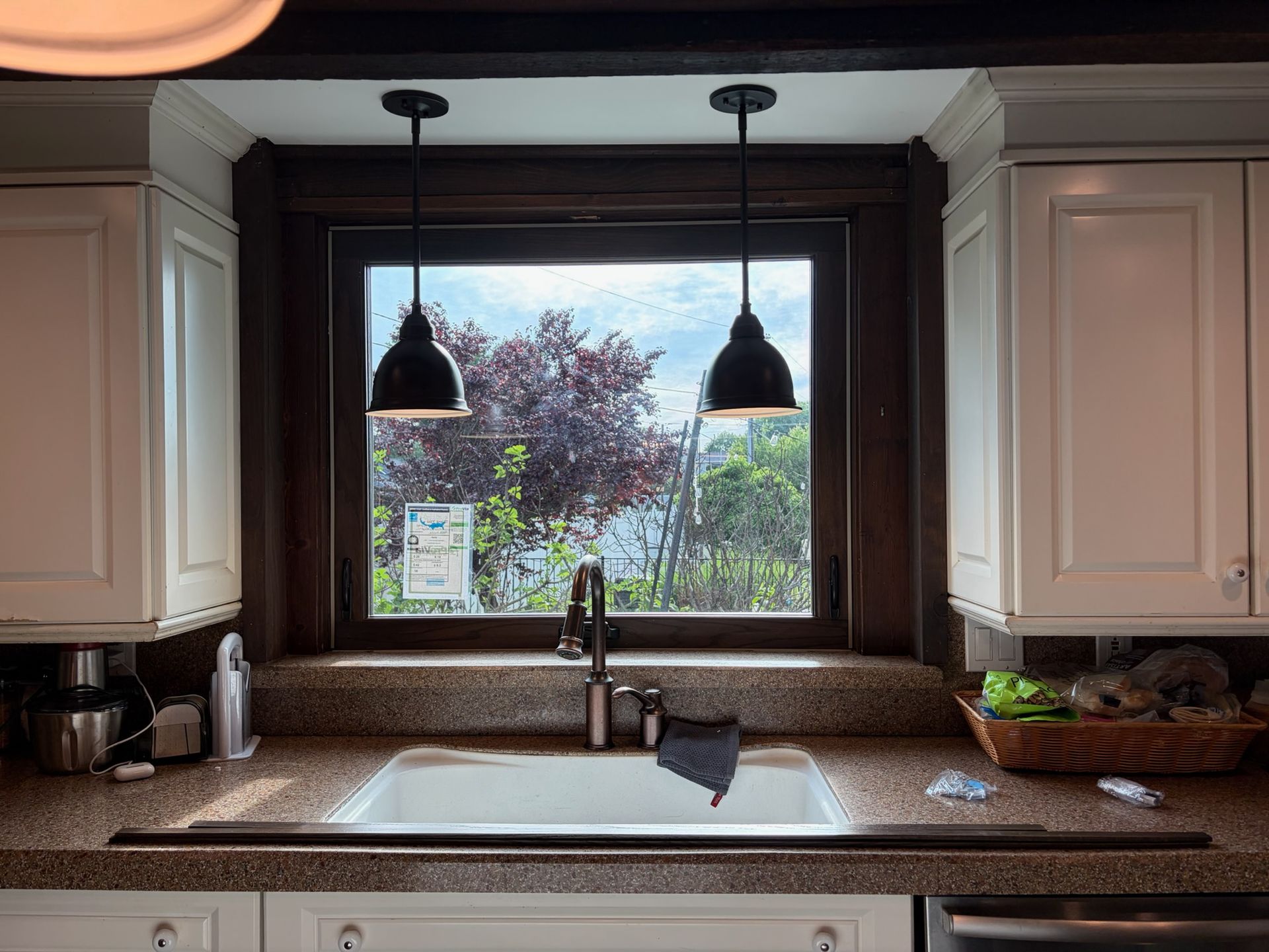 Kitchen sink under a window with two pendant lights and beige cabinets