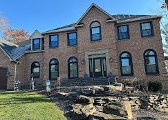 Two-story brick house with arched windows, front steps, and a stone retaining wall in a yard