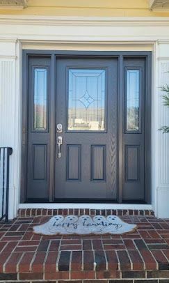 Front porch with a dark gray front door and sidelights above a brick step and doormat.