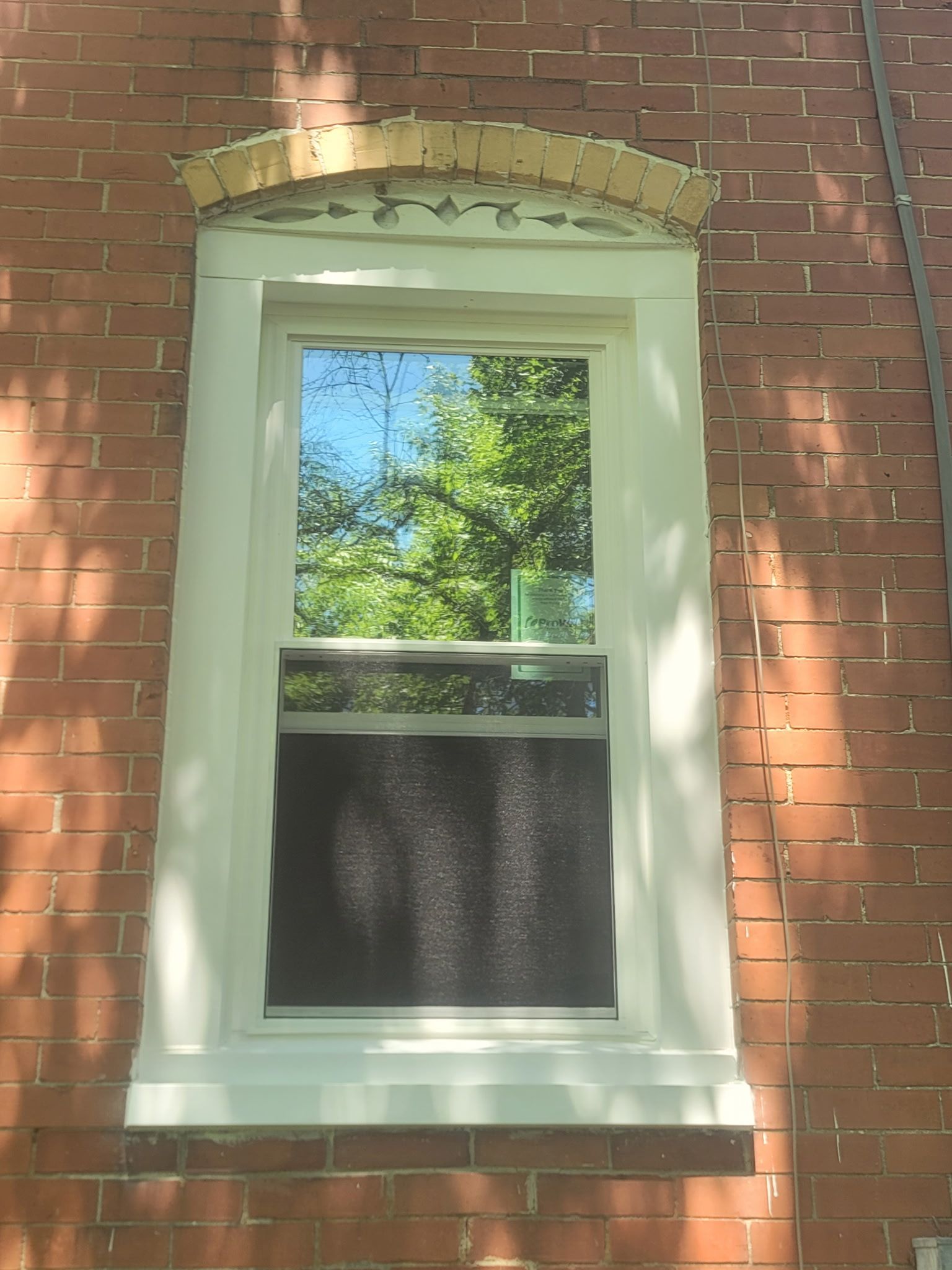 White-trimmed window on a red brick wall with a decorative brick arch above it.