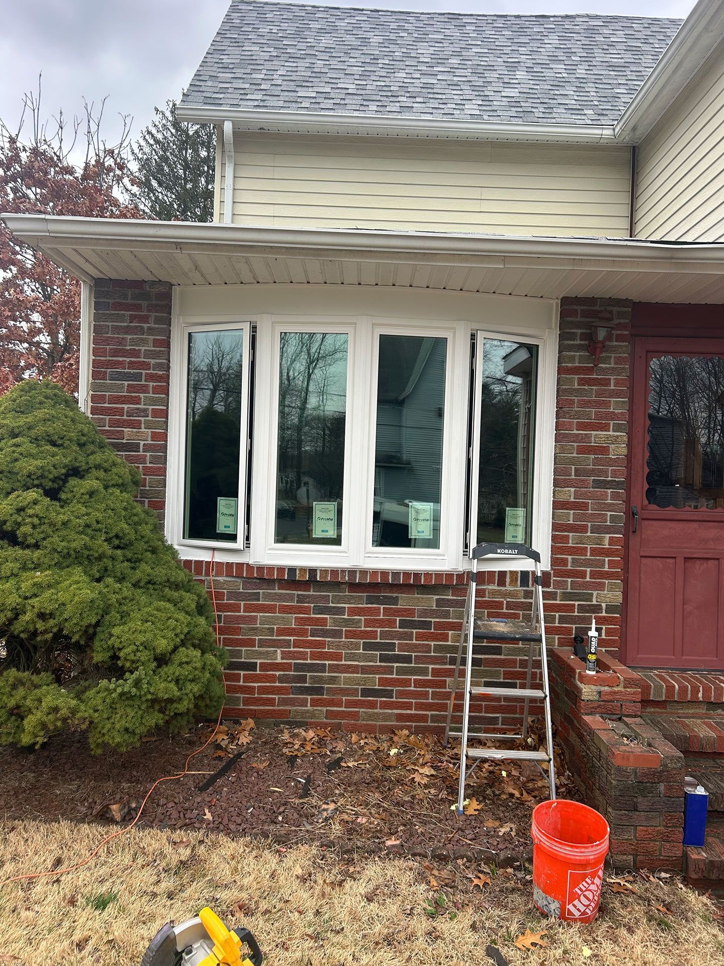 Brick house exterior with a white bay window, ladder, and orange bucket in front