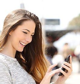 Woman smiling, looking at phone, outdoors.