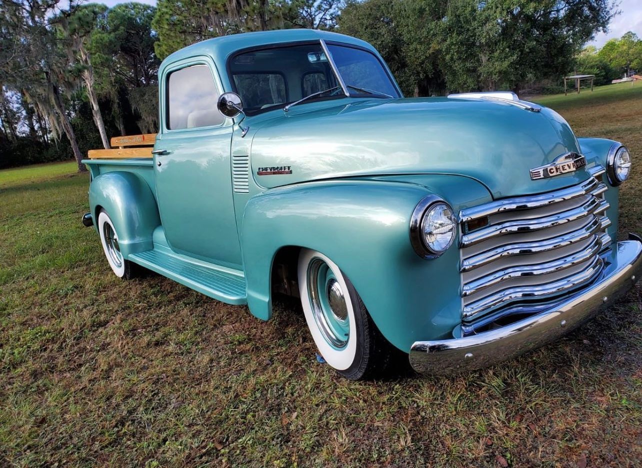 A blue pickup truck is parked in a grassy field.