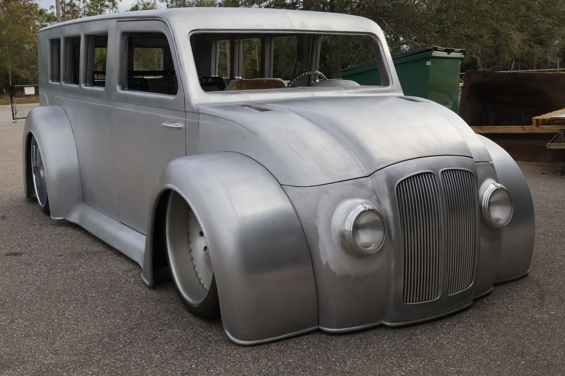 Sleek, silver custom hot rod car with rounded fenders and lowered suspension parked outside.
