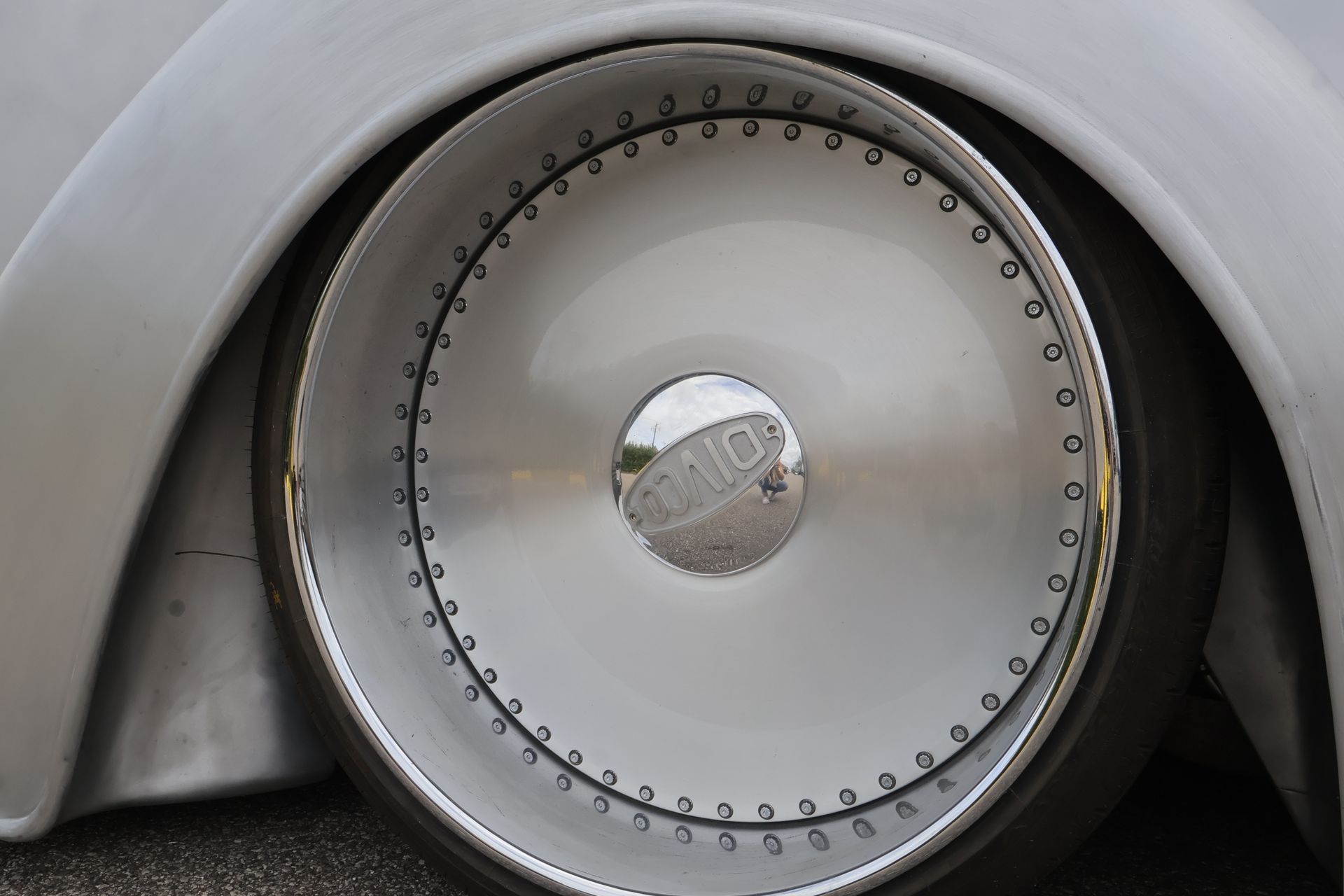 Chrome wheel on a lowered car with silver body, showing detailed bolts and a reflective hubcap.