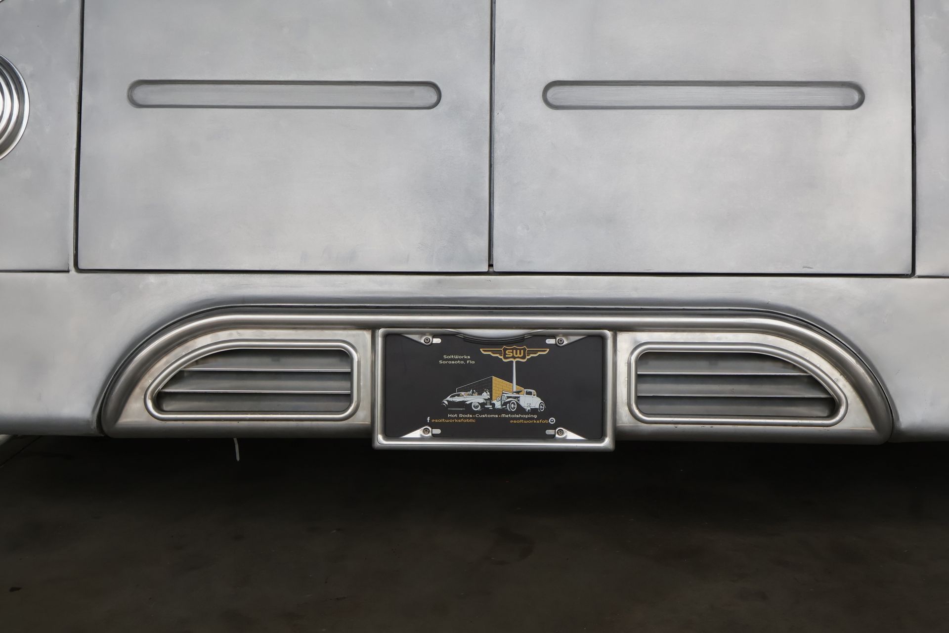 Close-up of a silver vehicle's rear with a license plate featuring a black and gold illustration.