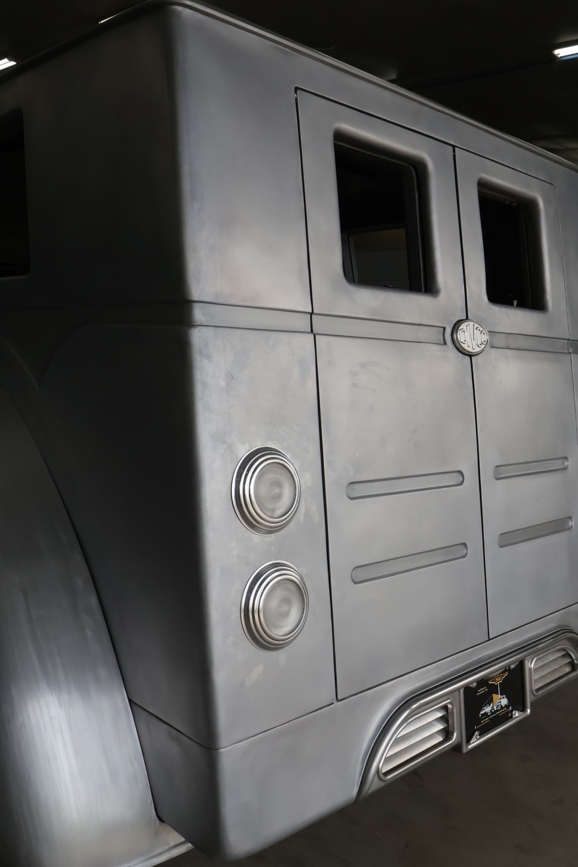 Rear view of a matte gray armored truck with two small windows and chrome tail lights.