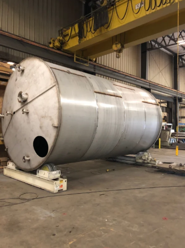 Large cylindrical metal tank in a factory, suspended by a yellow crane.