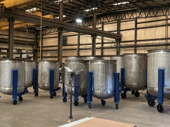 Stainless steel industrial tanks on wheels inside a large warehouse.