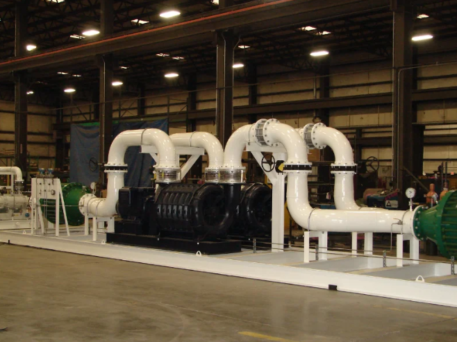 Large industrial equipment with black and white pipes, situated inside a warehouse.