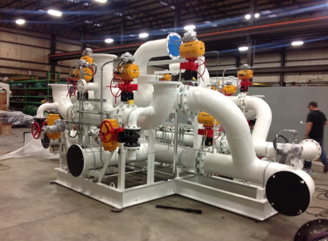 White industrial piping system with valves, set in a warehouse. A person walks nearby.