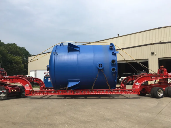 Large blue industrial tank secured to a red flatbed trailer outdoors.