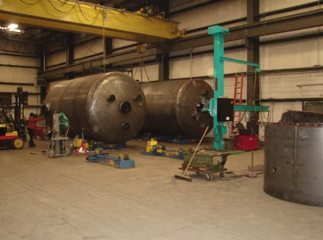 Two large industrial tanks inside a warehouse, with machinery and workers.