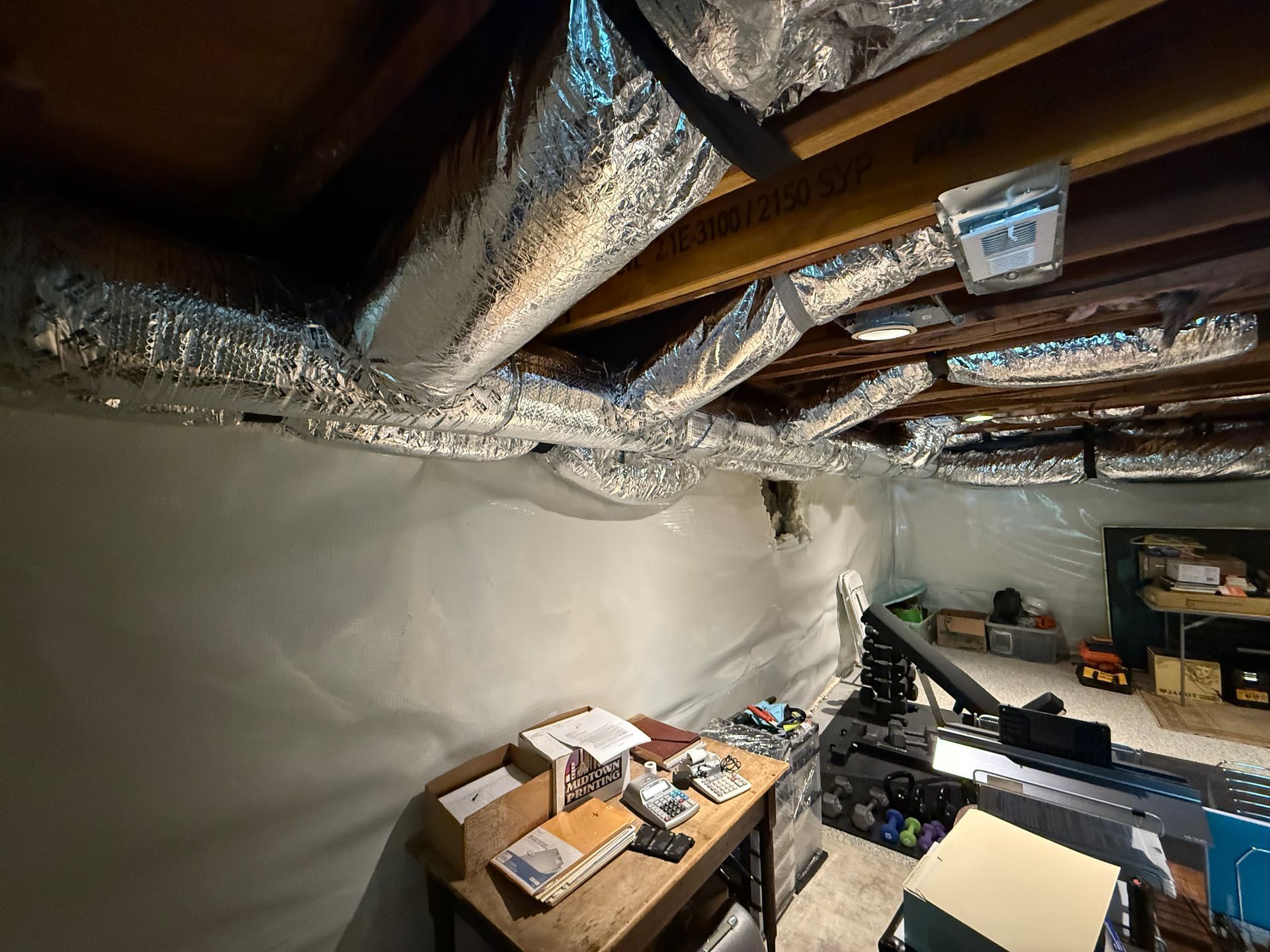 Basement with silver ductwork, white walls, a workbench, and various items.