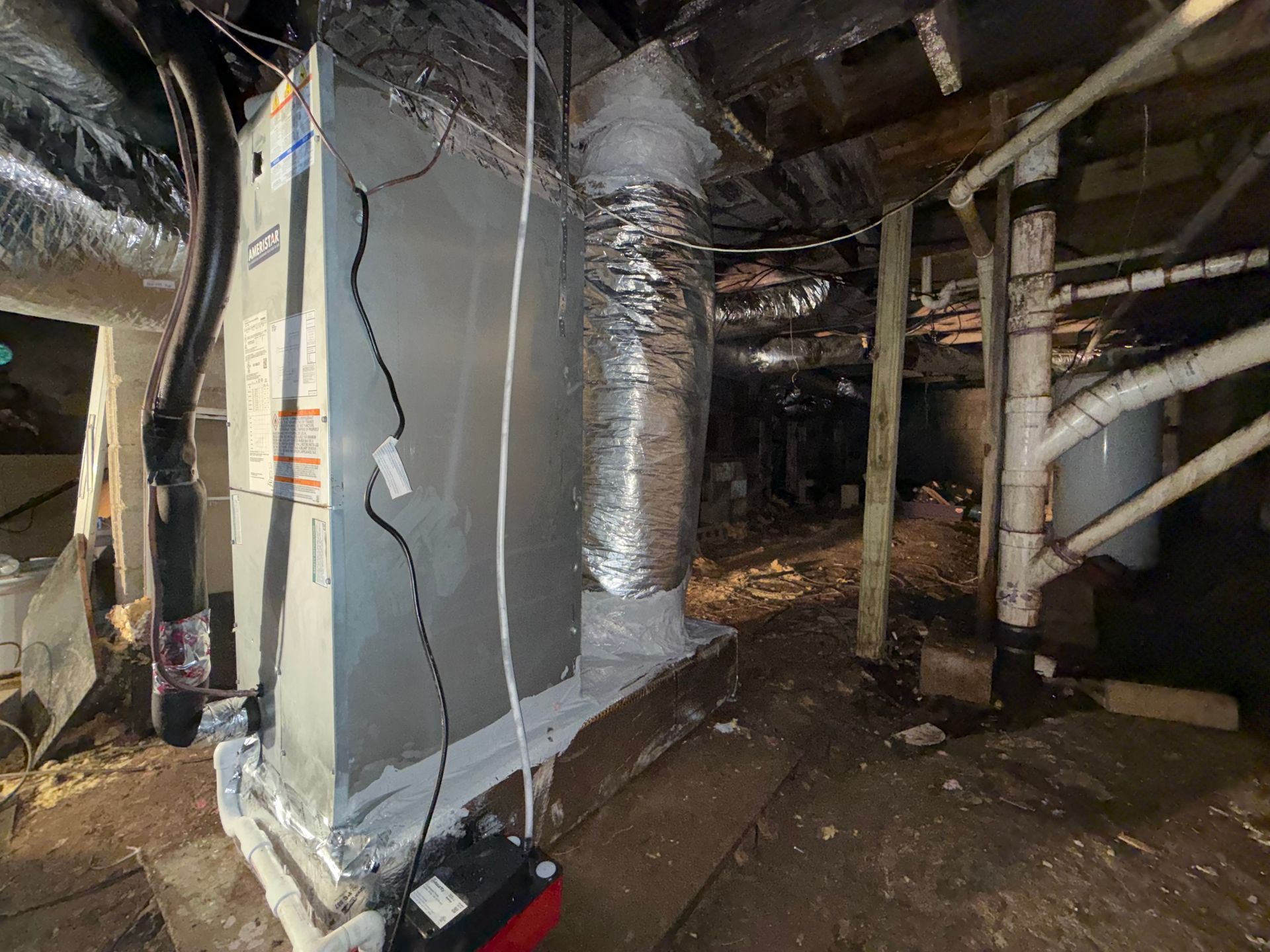 HVAC system in a crawl space, with ductwork and a red condensate pump.