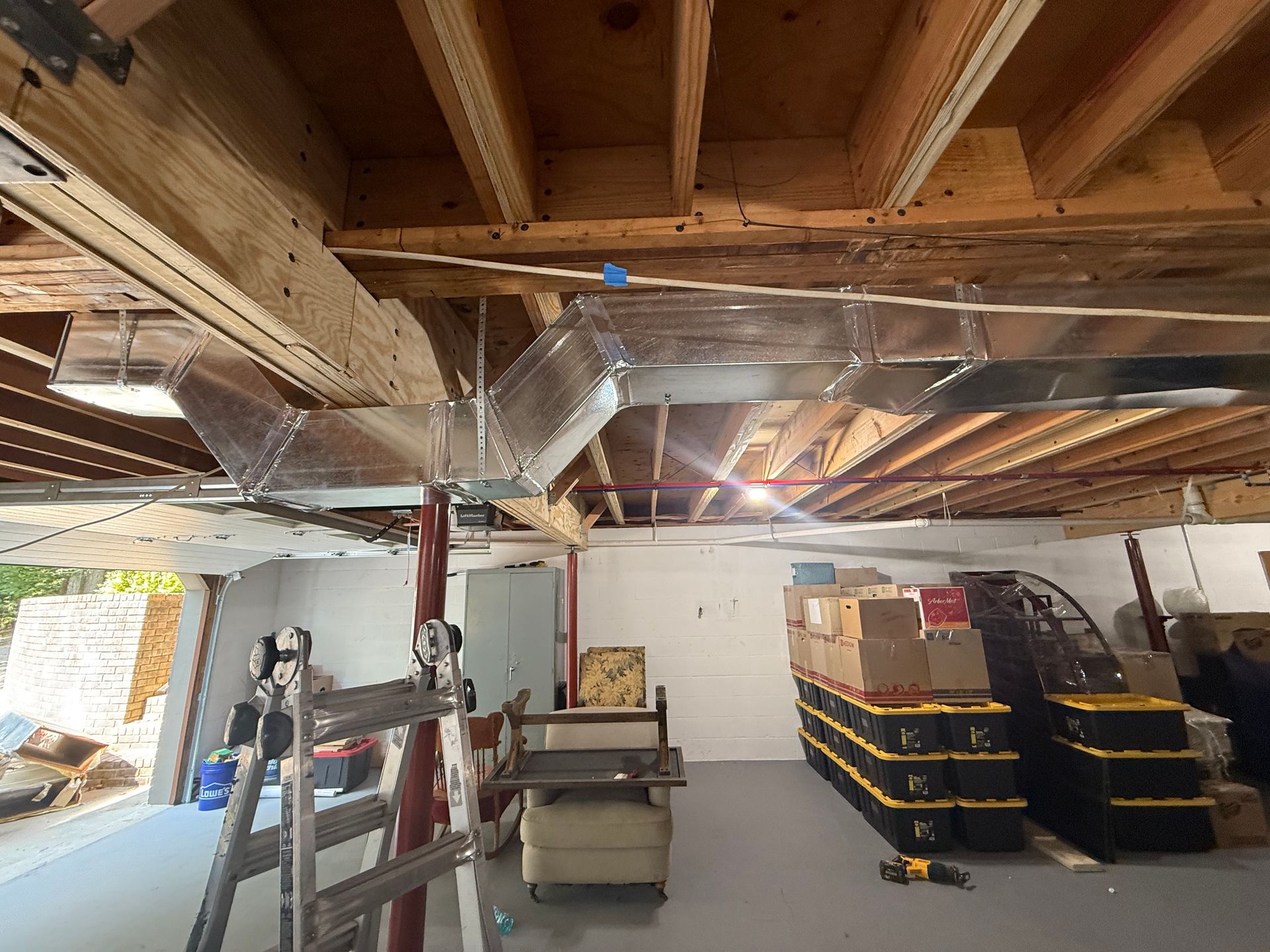 Basement with ductwork installed along the ceiling, with storage and a ladder visible.