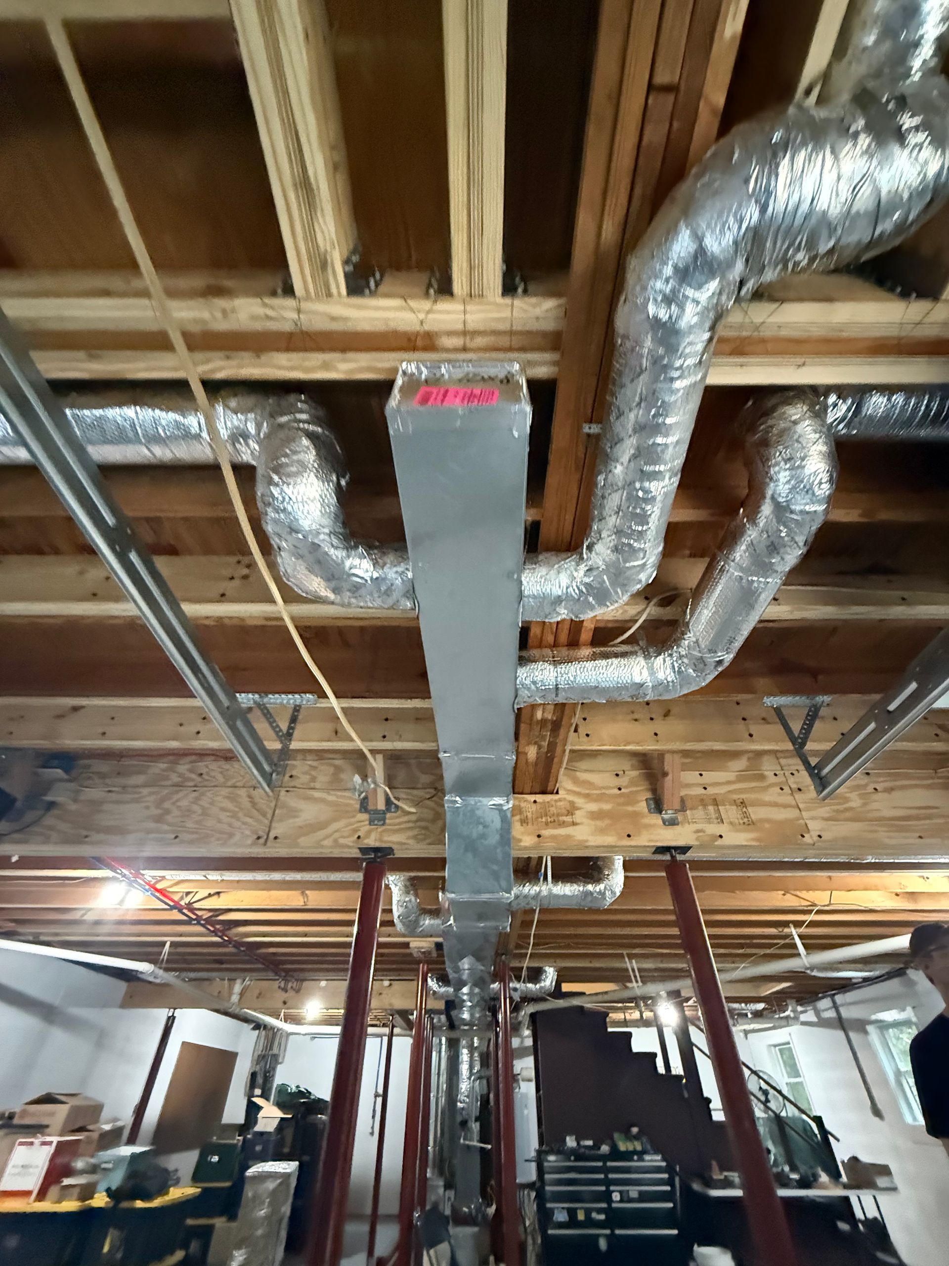HVAC ductwork and flexible vents installed in a basement ceiling, wooden beams, metal support beams visible.