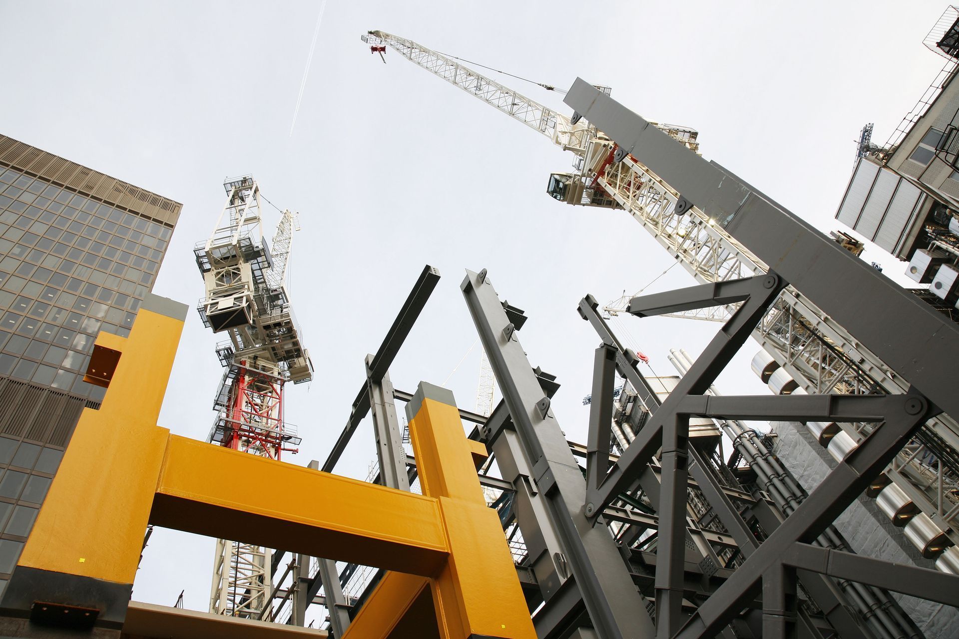 Construction site with cranes and yellow and gray steel beams against a cloudy sky.