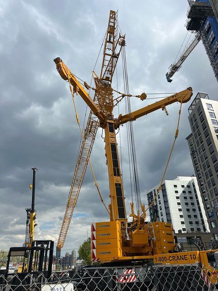 Yellow crane at a construction site against a cloudy sky. Buildings are in the background.