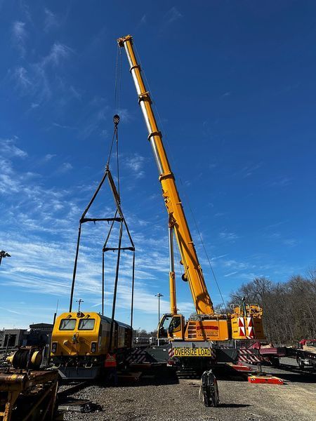 Yellow crane lifting a yellow and black rail car under a blue sky.