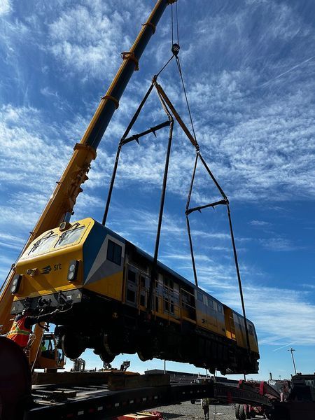 Crane lifting a yellow and blue train car against a blue sky.