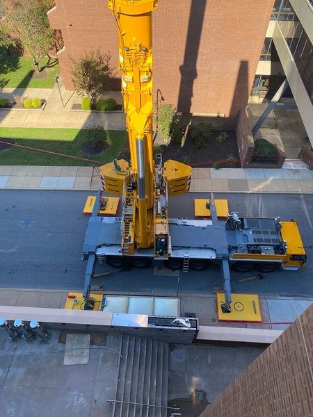 A large yellow crane positioned on a street, likely for construction near a brick building.