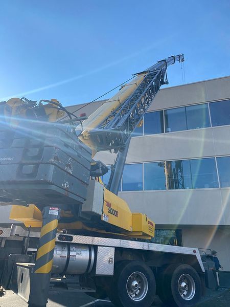 Yellow crane extending towards a building with blue-tinted windows against a bright blue sky.