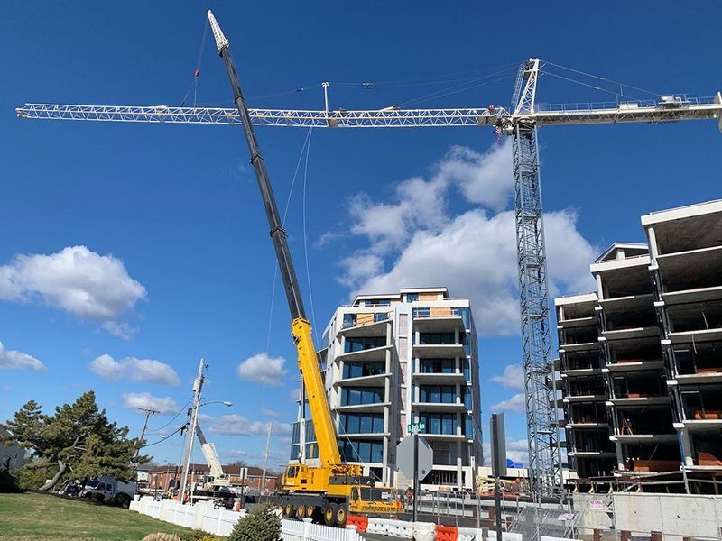 Construction site with a yellow mobile crane and a tower crane, both against a partially built building and a bright blue sky.