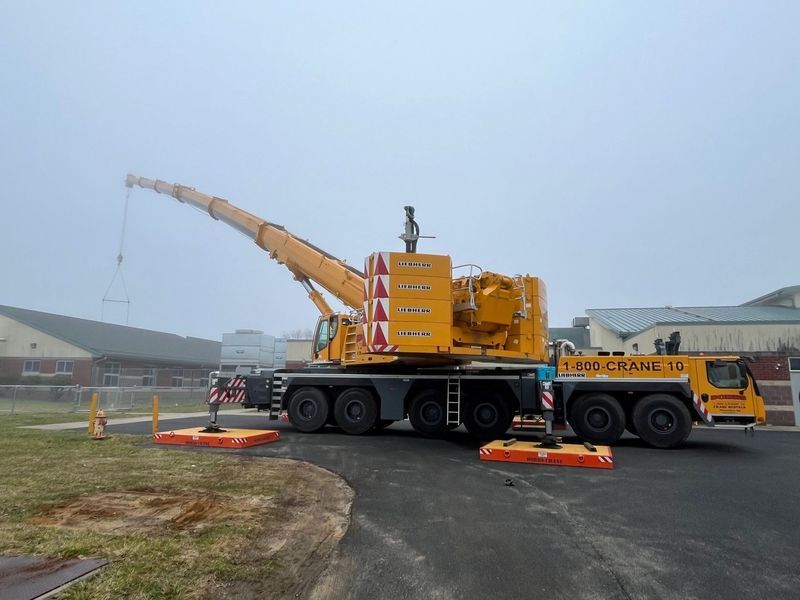 Yellow mobile crane parked near a building on a foggy day.