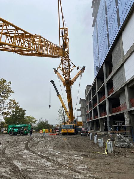 Yellow crane lifting near a building under construction, cloudy sky overhead.