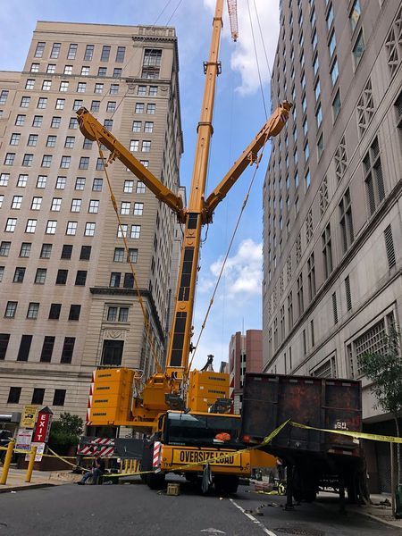 A large yellow crane positioned between two tall buildings, next to a black trailer, cordoned off with caution tape.