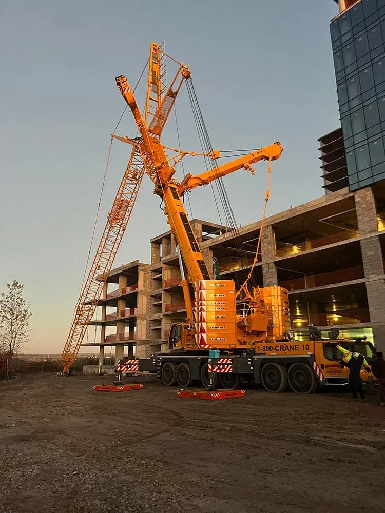Large yellow construction crane lifting near a partially built concrete building under a blue sky.