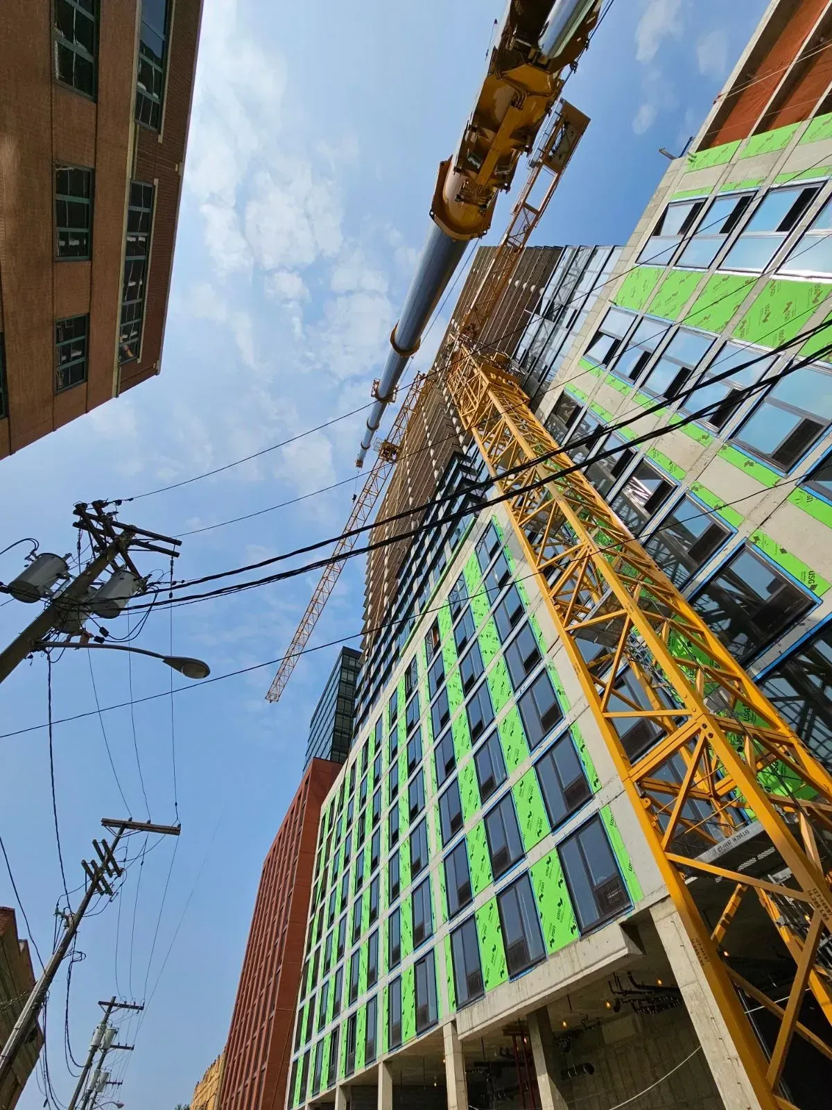 Construction site with crane reaching toward blue sky and buildings in progress.