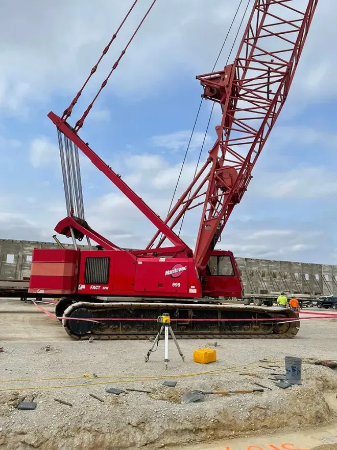 Red crane on a construction site; the boom is raised. Cloudy sky in the background.