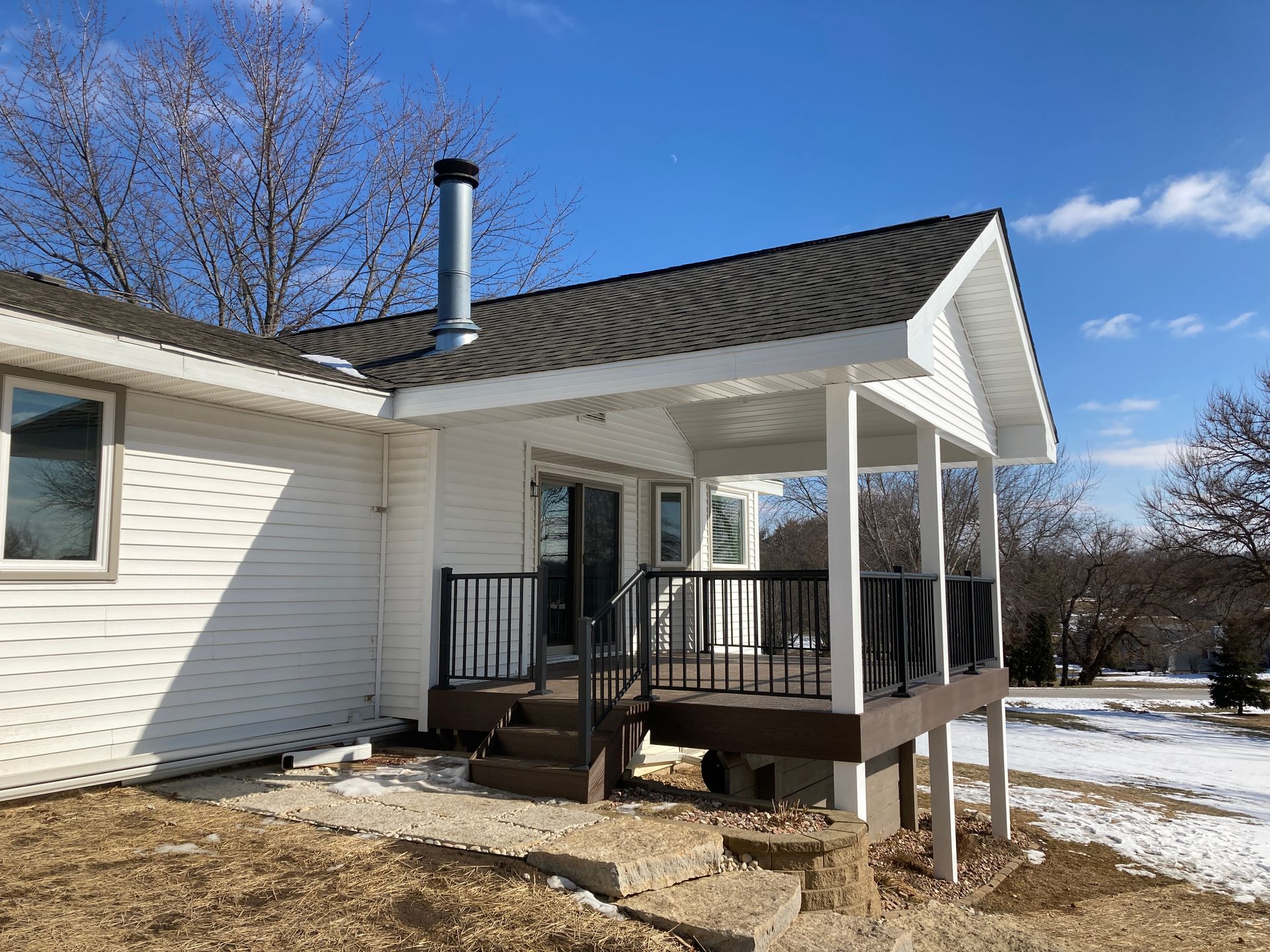 White house with a brown deck and black railing under a white covered porch, sunny day.