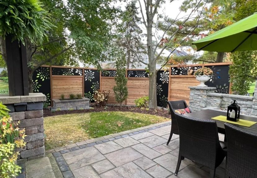Patio with stone pavers, wooden fence with decorative panels, and green umbrella.