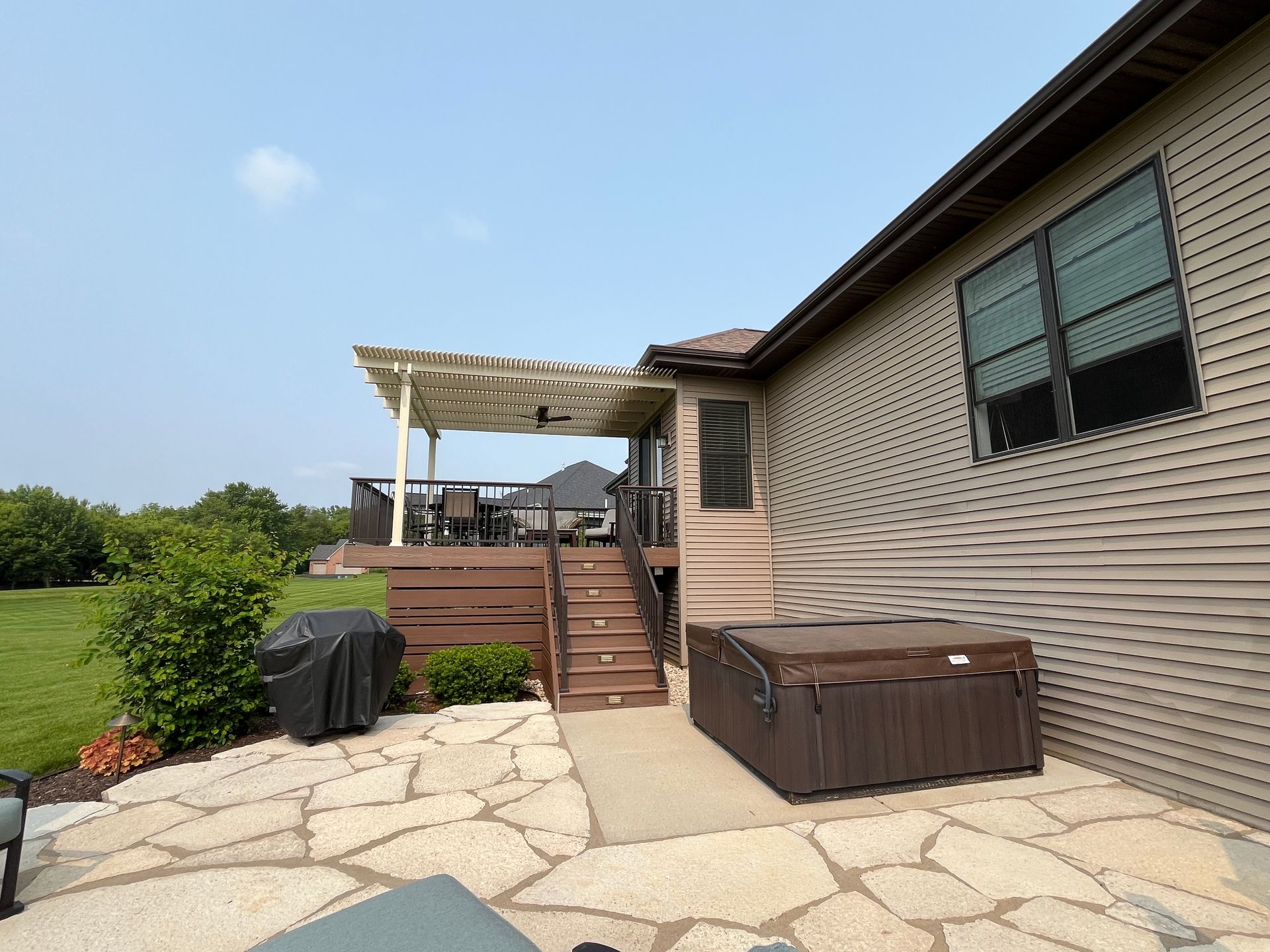 Backyard patio with a hot tub, wooden deck with pergola, and a house with brown siding.