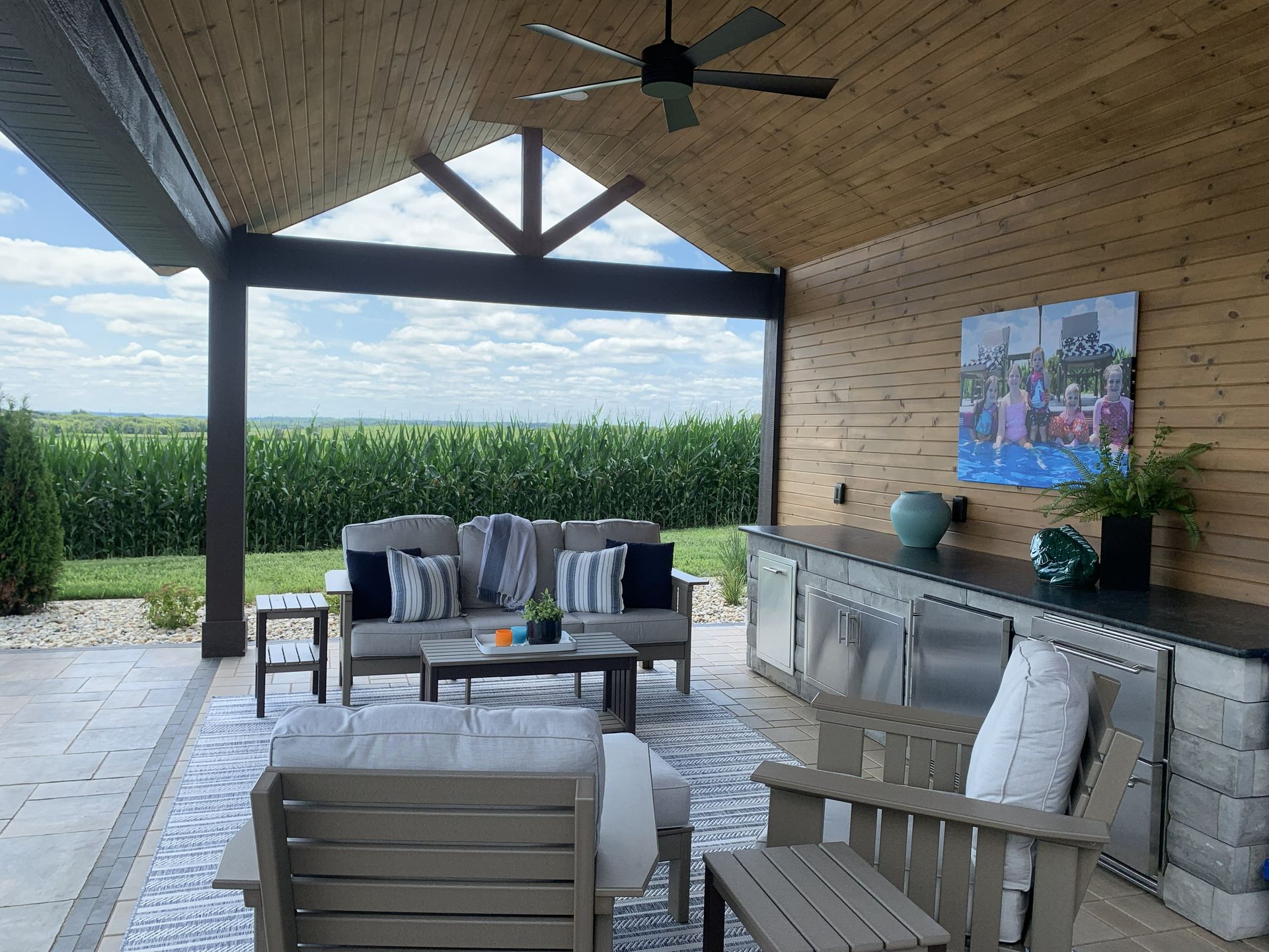 Covered outdoor patio with seating, built-in bar, and view of a cornfield.