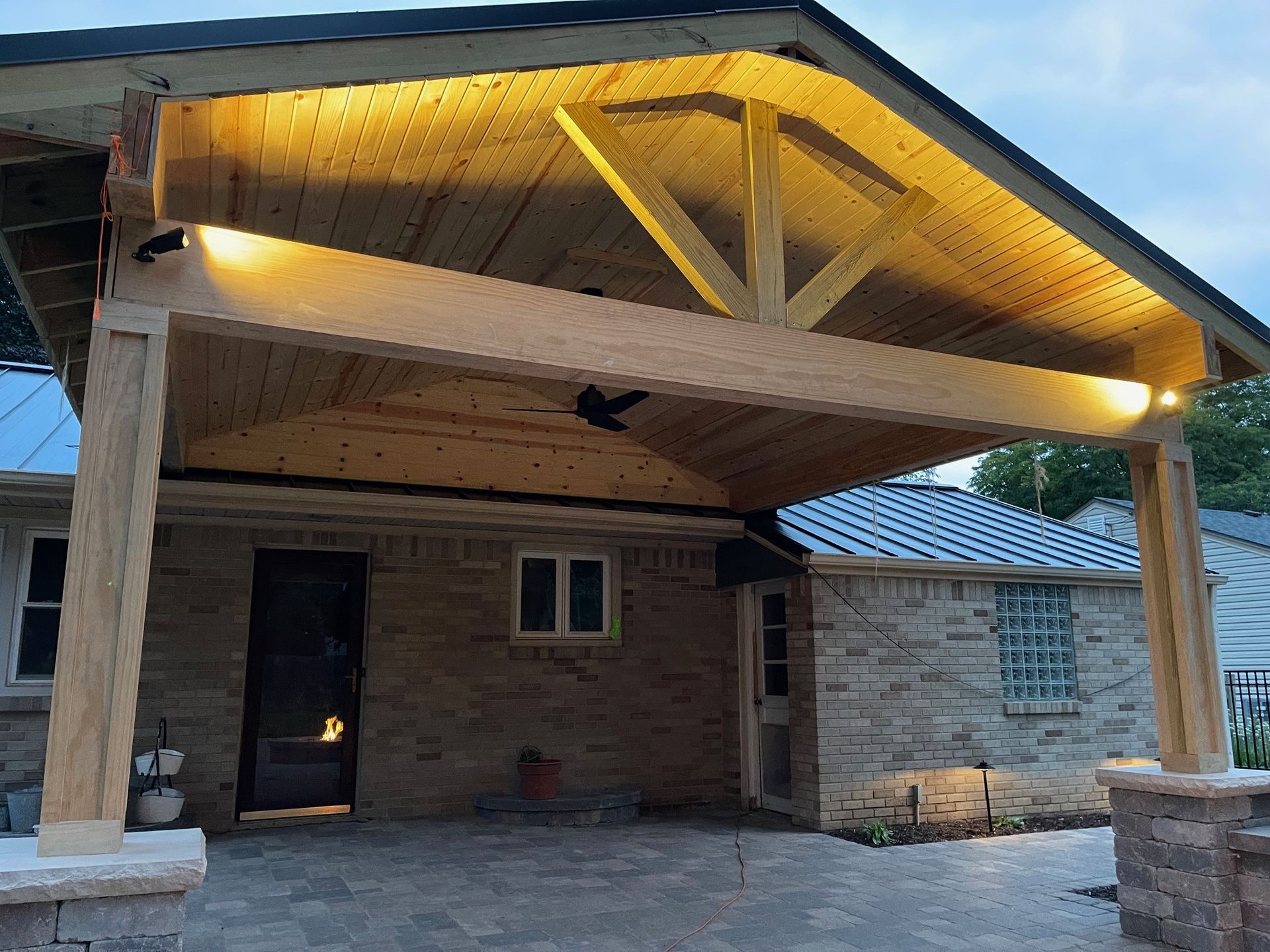 Wooden patio cover with built-in lights over a brick house. Nighttime view.